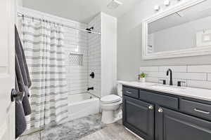 Full bath with shower / bathtub combination with curtain, light wood finished floors, vanity, a textured ceiling, and tasteful backsplash