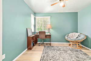 Home office featuring light wood-style floors, a textured ceiling, and a ceiling fan