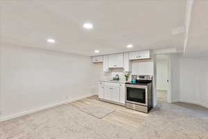 Kitchen with stainless steel electric stove, white cabinetry, light countertops, a textured ceiling, and light colored carpet