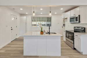 Kitchen with stainless steel appliances, white cabinets, recessed lighting, hanging light fixtures, and light wood-type flooring