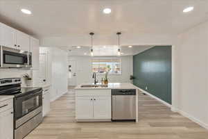Kitchen with appliances with stainless steel finishes, white cabinets, recessed lighting, hanging light fixtures, and a kitchen island with sink