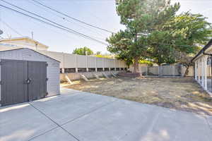 Fenced backyard featuring a storage unit and a patio area