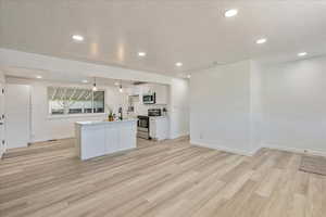 Kitchen featuring white cabinetry, a center island, a textured ceiling, appliances with stainless steel finishes, and pendant lighting