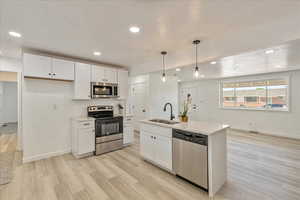 Kitchen with appliances with stainless steel finishes, white cabinets, decorative light fixtures, light wood finished floors, and recessed lighting