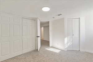 Unfurnished bedroom featuring light carpet, multiple closets, and a textured ceiling