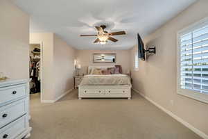 Owner's suite bedroom featuring light carpet, a walk in closet, and a ceiling fan