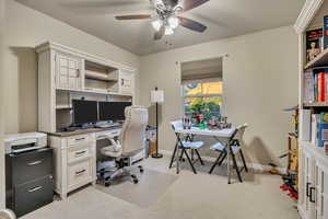Bedroom being used as an office light colored carpet and ceiling fan
