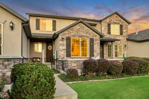 View of front facade with stone siding, stucco siding, and a front lawn