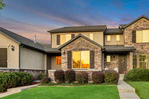 View of front facade with stone siding, a lawn, stucco siding, and a shingled roof