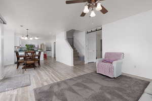 Living area featuring a barn door, stairway, light wood finished floors, a ceiling fan, and a chandelier