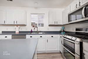Kitchen featuring appliances with stainless steel finishes, dark countertops, white cabinets, and light wood-style floors