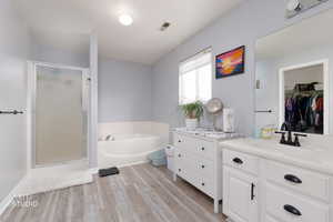 Full bath with a walk in closet, vanity, a bath, light wood-style flooring, and a shower stall