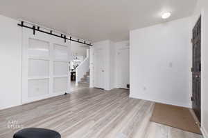 Unfurnished living room with a barn door, light wood-style floors, and stairway