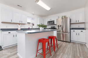 Kitchen with dark countertops, stainless steel appliances, white cabinets, and light wood-style floors