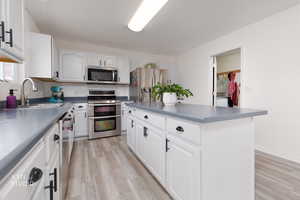 Kitchen featuring white cabinetry, stainless steel appliances, light wood finished floors, dark countertops, and a center island
