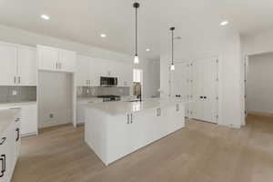 Kitchen with decorative light fixtures, white cabinetry, recessed lighting, light wood finished floors, and appliances with stainless steel finishes