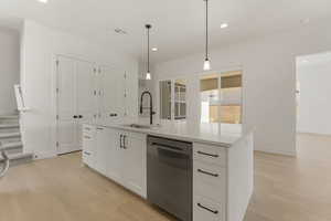 Kitchen featuring pendant lighting, white cabinetry, stainless steel dishwasher, light wood-style floors, and an island with sink
