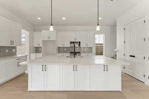 Kitchen featuring hanging light fixtures, white cabinetry, light wood finished floors, light stone countertops, and recessed lighting