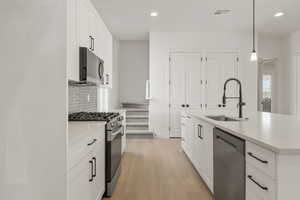 Kitchen with decorative light fixtures, appliances with stainless steel finishes, white cabinetry, light wood-style floors, and recessed lighting