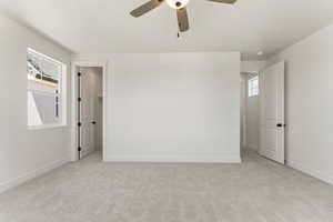 Unfurnished bedroom featuring light colored carpet, a walk in closet, and ceiling fan