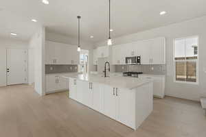 Kitchen featuring tasteful backsplash, hanging light fixtures, an island with sink, white cabinets, and light wood finished floors