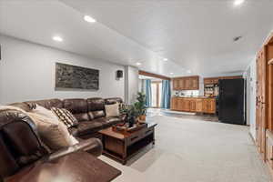 Living room with light colored carpet, recessed lighting, and bar with sink