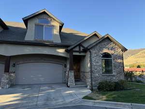 View of front facade with stone siding, a garage, concrete driveway, and roof with shingles