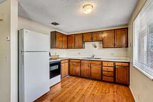 Kitchen featuring freestanding refrigerator, light countertops, range with electric cooktop, brown cabinets, and light wood-style floors