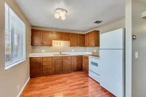 Kitchen with white appliances, light countertops, brown cabinets, light wood-style floors, and a textured ceiling