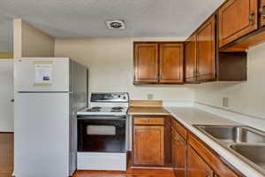Kitchen with white appliances, brown cabinetry, a textured ceiling, light countertops, and light wood-style flooring