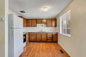 Kitchen with freestanding refrigerator, light countertops, brown cabinetry, a textured ceiling, and light wood-style floors