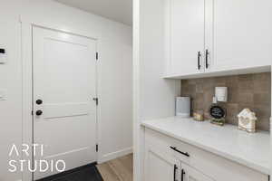 Bar featuring white cabinetry, light stone counters, light wood-style flooring, and decorative backsplash