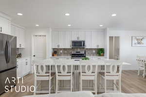 Kitchen with a kitchen breakfast bar, light wood-style flooring, appliances with stainless steel finishes, and recessed lighting