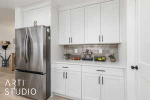 Kitchen featuring freestanding refrigerator, white cabinets, light stone counters, and backsplash