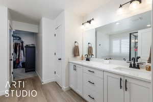 Primary bathroom featuring double vanity, light wood finished floors, and a walk in closet