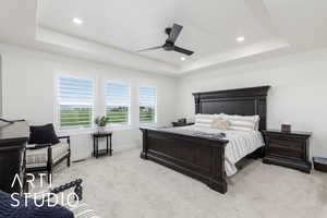 Primary bedroom with a raised ceiling, light carpet, ceiling fan, and recessed lighting