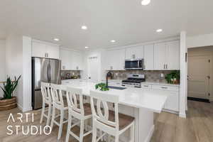Kitchen featuring white cabinets, a kitchen bar, appliances with stainless steel finishes, a kitchen island with sink, and backsplash