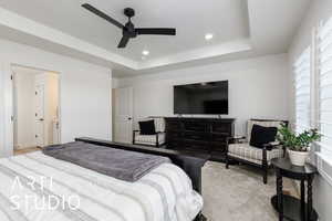 Primary bedroom with a tray ceiling, a ceiling fan, recessed lighting, and light colored carpet