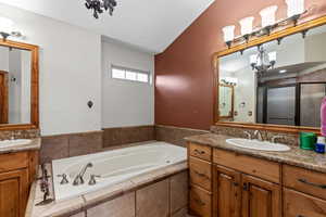 Full bathroom with two vanities, a garden tub, vaulted ceiling, a chandelier, and a shower stall