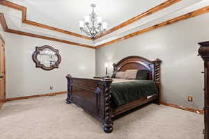 Bedroom with ornamental molding, light carpet, a tray ceiling, and a chandelier
