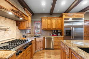 Kitchen featuring decorative backsplash, custom range hood, appliances with stainless steel finishes, beam ceiling, and light wood finished floors