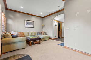 Carpeted living area with arched walkways, ornamental molding, and recessed lighting