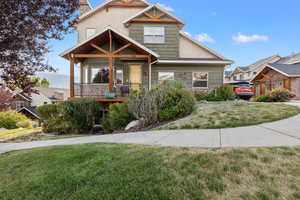 Craftsman house with a front yard, stone siding, a chimney, and covered porch