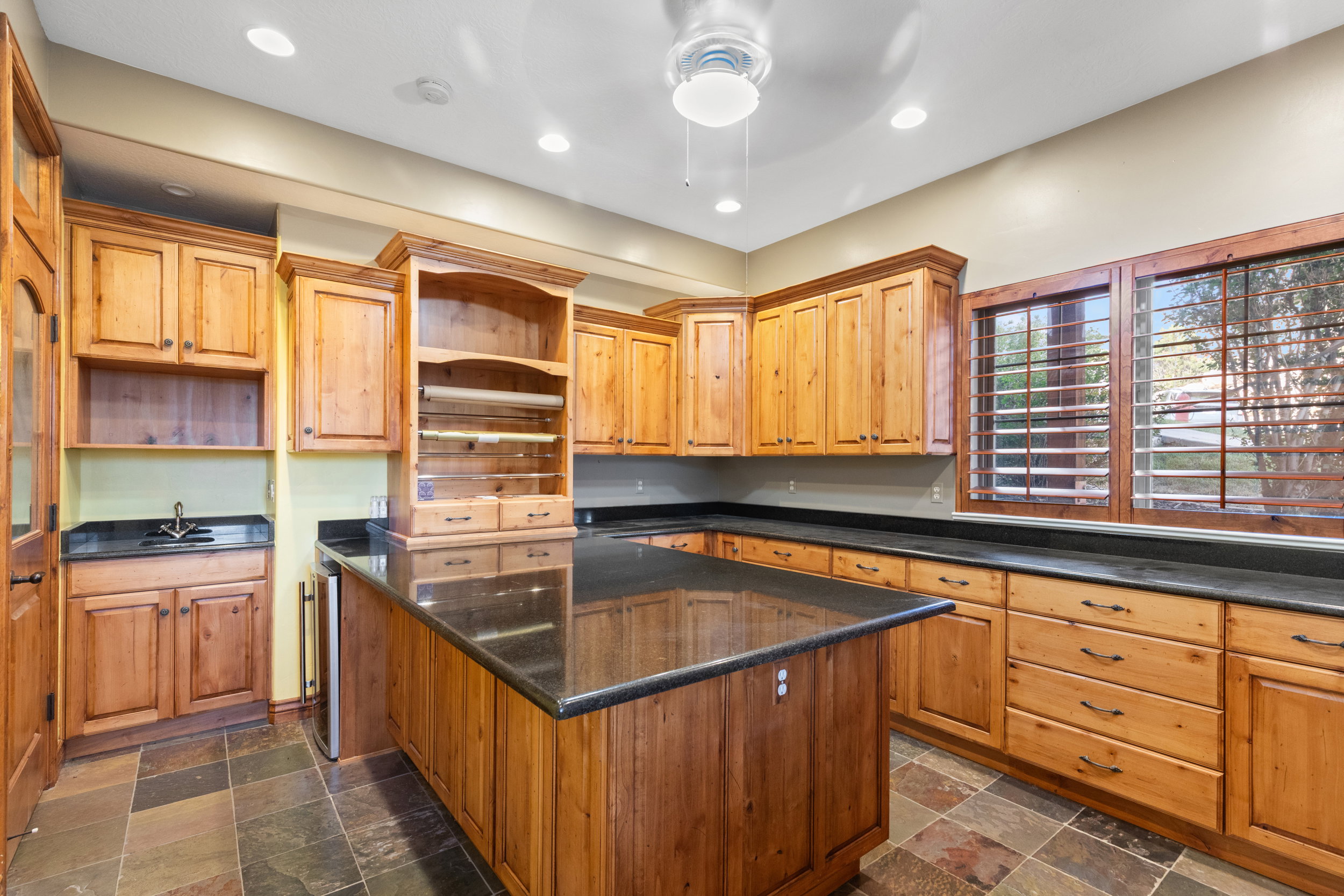 Kitchen featuring open shelves, a center island, recessed lighting, and dark stone finish floors