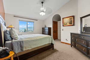 Bedroom featuring lofted ceiling, light carpet, arched walkways, and a ceiling fan