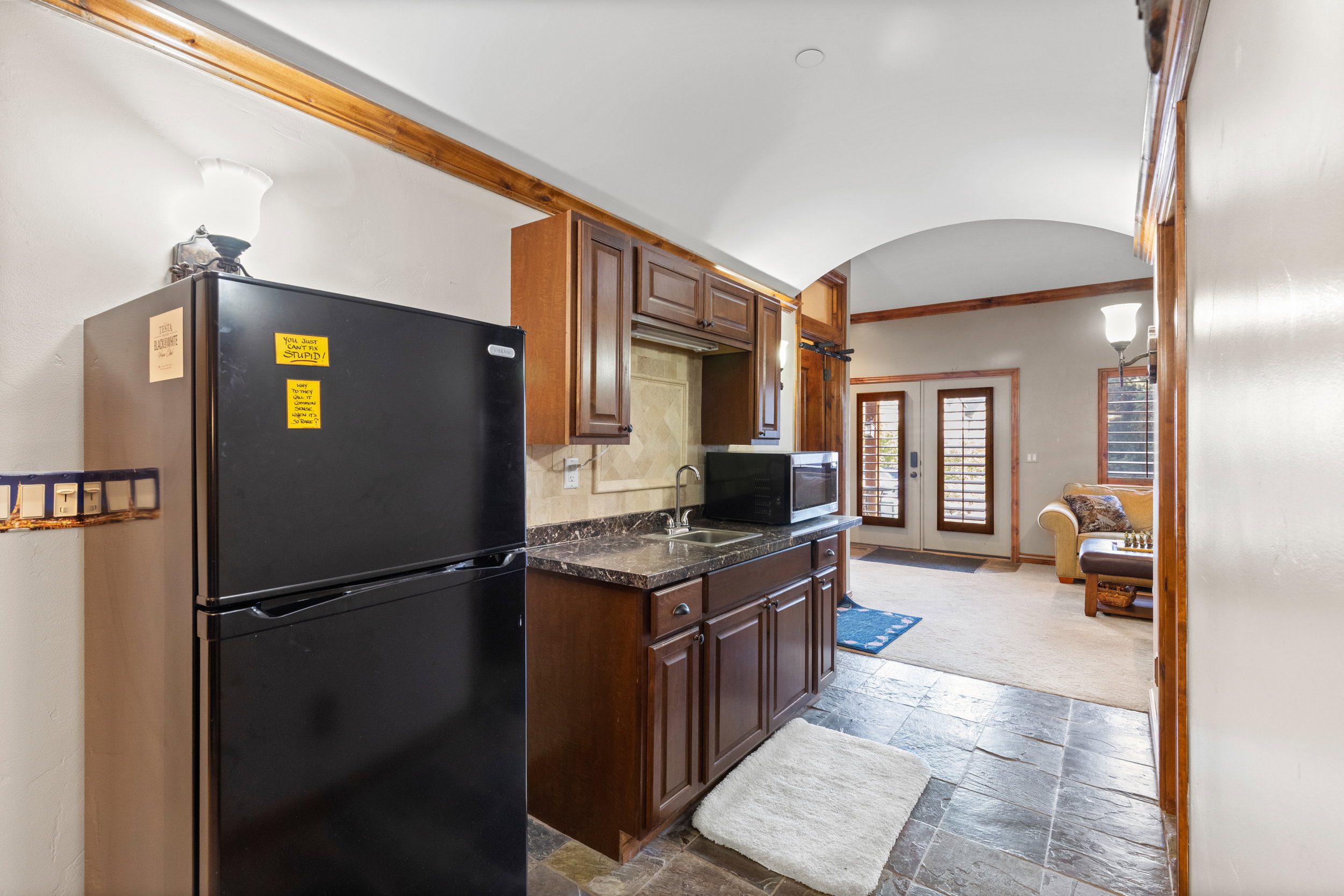 Kitchen with freestanding refrigerator, crown molding, stone tile flooring, stainless steel microwave, and arched walkways