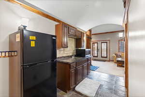Kitchen with freestanding refrigerator, crown molding, stone tile flooring, stainless steel microwave, and arched walkways