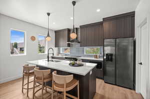 Kitchen with dark grey cabinetry, black stainless appliances, tasteful backsplash, a breakfast bar area, and an island with sink