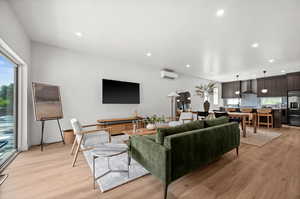 Living area with light wood finish LVP floors, recessed lighting, and a wall mounted air conditioner