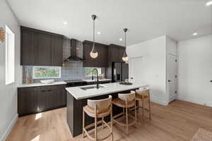 Kitchen with dark grey modern wood-look cabinets, a kitchen island, pantry, wall chimney exhaust hood, and tile backsplash
